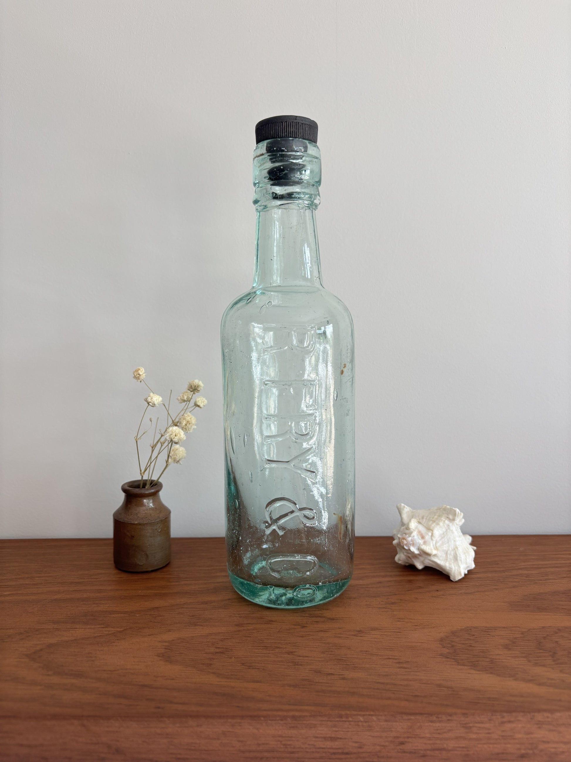 Clear glass bottle with a black cap on a wooden surface against a plain background