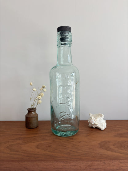 Clear glass bottle with a black cap on a wooden surface against a plain background