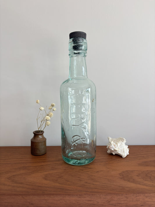 Clear glass bottle with a black cap on a wooden surface against a plain background