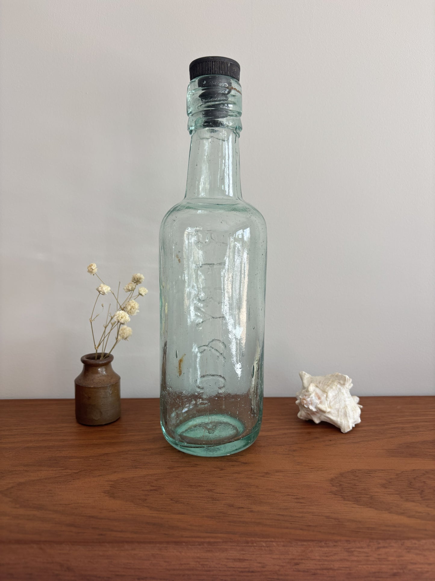 Clear glass bottle with a black cap on a wooden surface with decorative items.