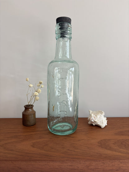 Clear glass bottle with a black cap on a wooden surface with decorative items.