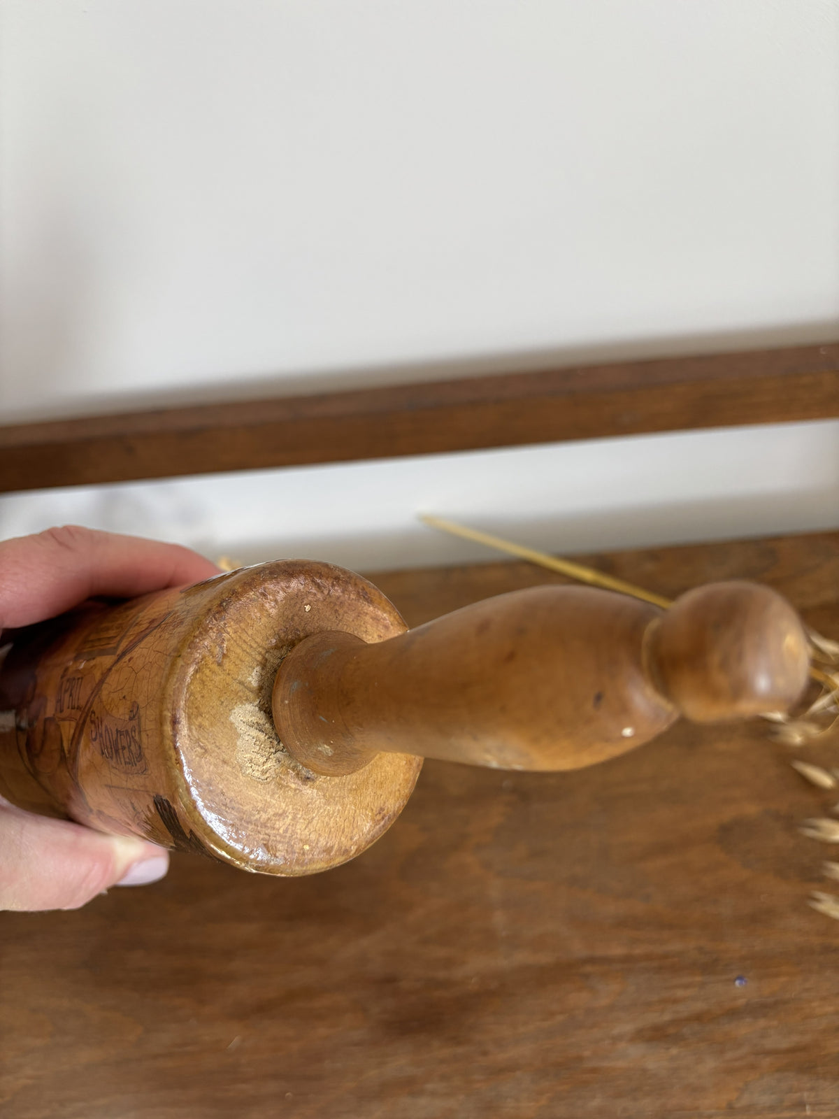 A close-up of a hand holding a vintage wooden rolling pin over a rustic wooden table.