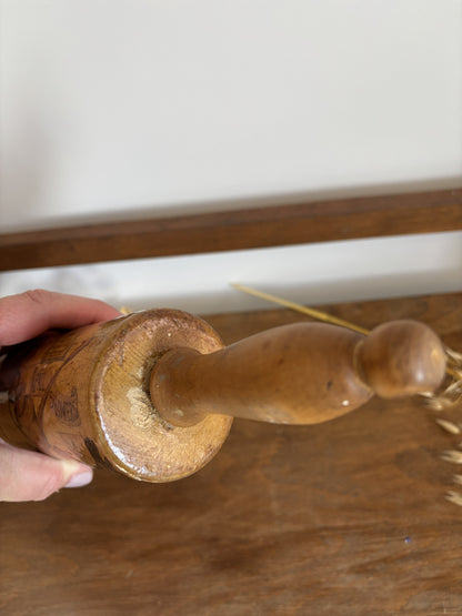 A close-up of a hand holding a vintage wooden rolling pin over a rustic wooden table.