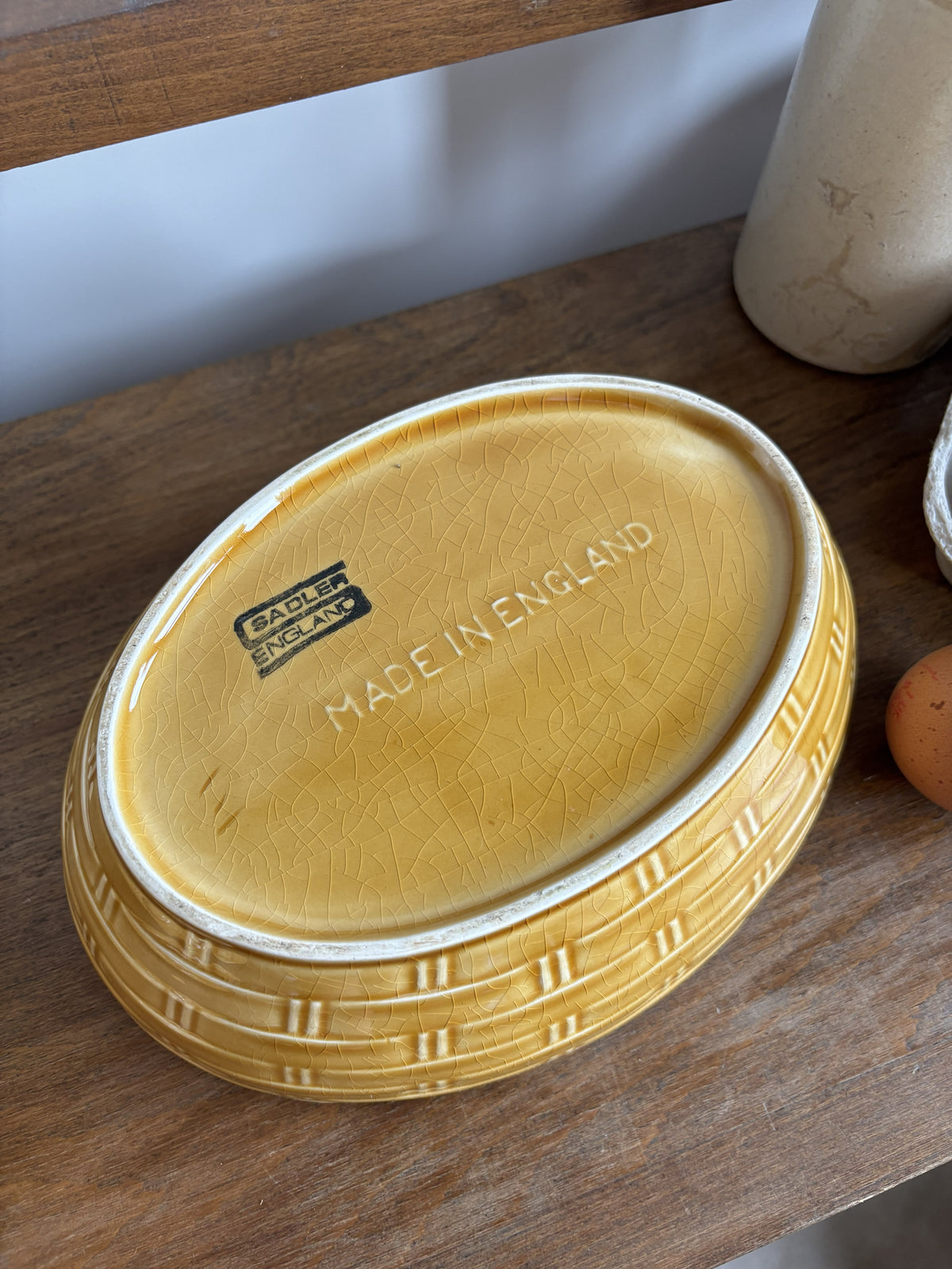 The base of a honey yellow/brown glazed ceramic hen on nest egg keeper.  The words Sadler England and Made in England are printed on the bottom.  