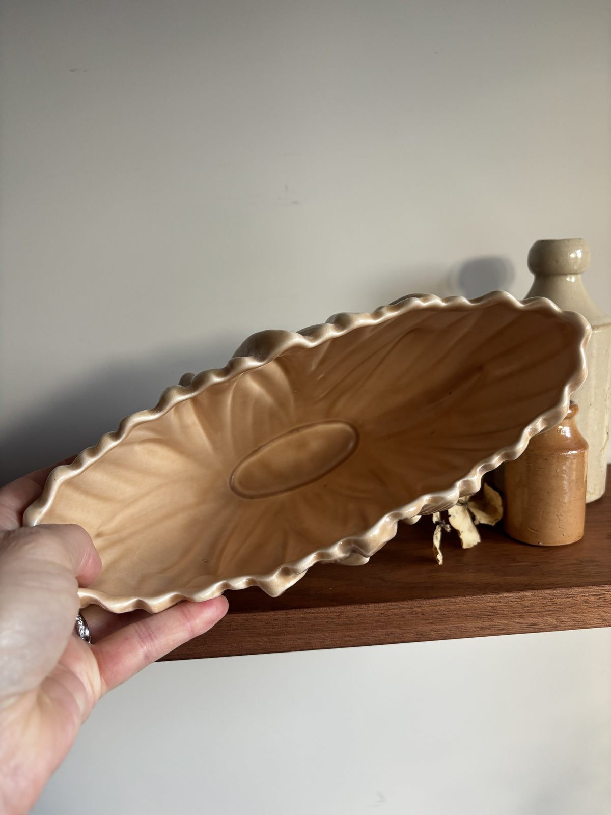 The inside of a vintage fawn coloured SylvaC vase set against a neutral background with a wooden shelf and small decorative bottles.