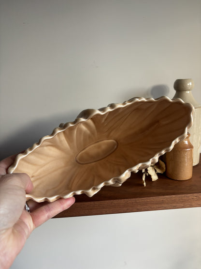 The inside of a vintage fawn coloured SylvaC vase set against a neutral background with a wooden shelf and small decorative bottles.