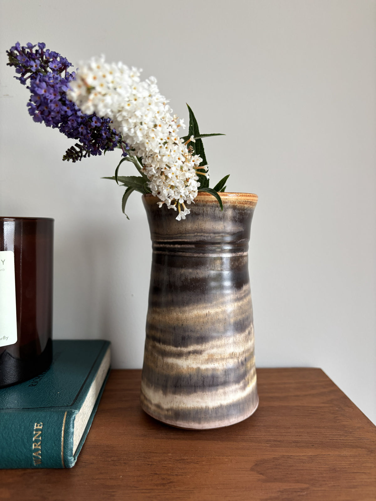 A brown glazed bud vase containing white and purple flowers. 
