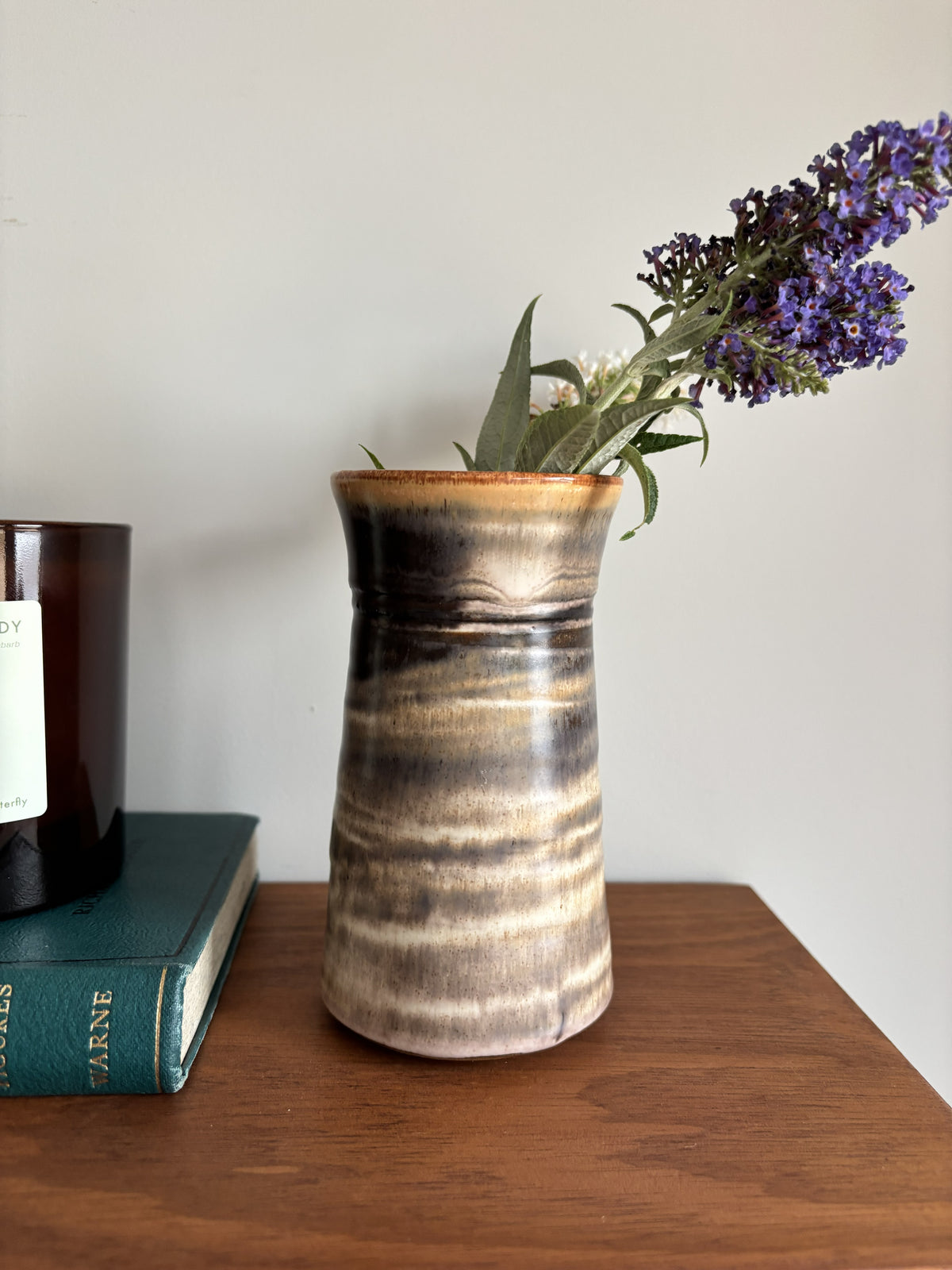 A brown bud vase containing purple flowers