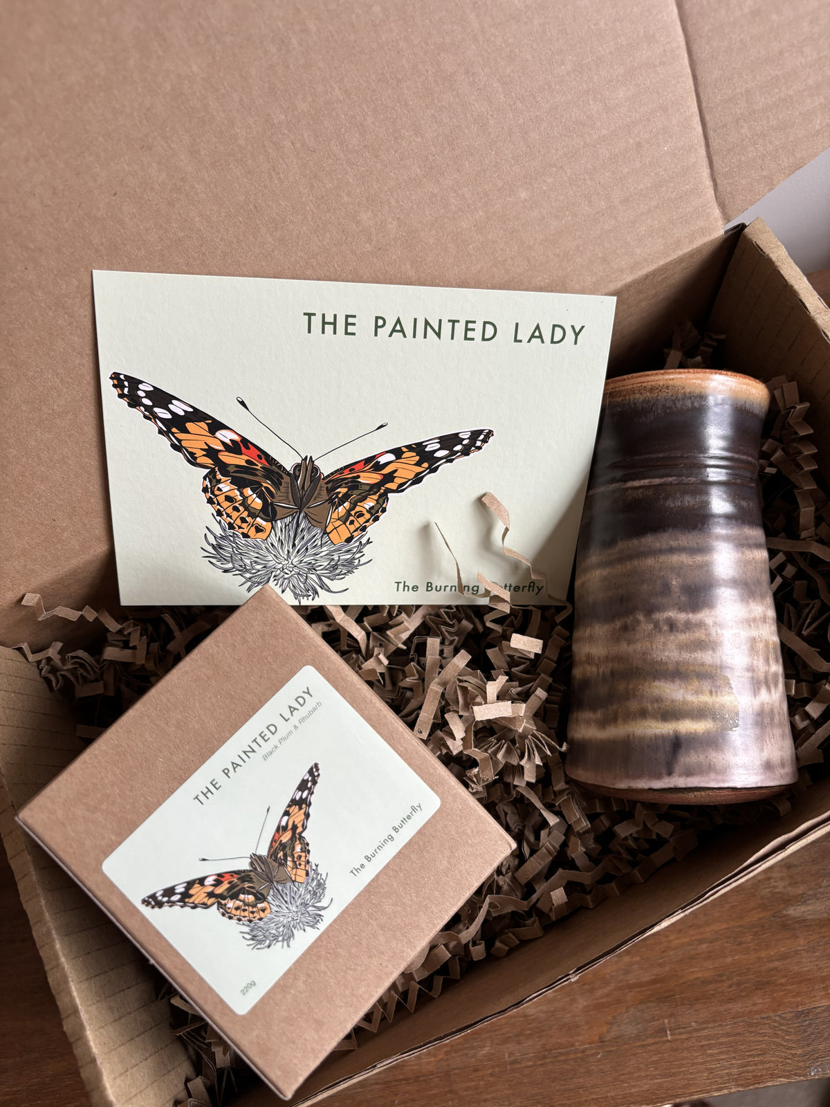 A gift box from The Burning Butterfly containing The Painted Lady candle in a kraft gift box, a small brown bud vase and The Painted Lady butterfly A6 postcard. 