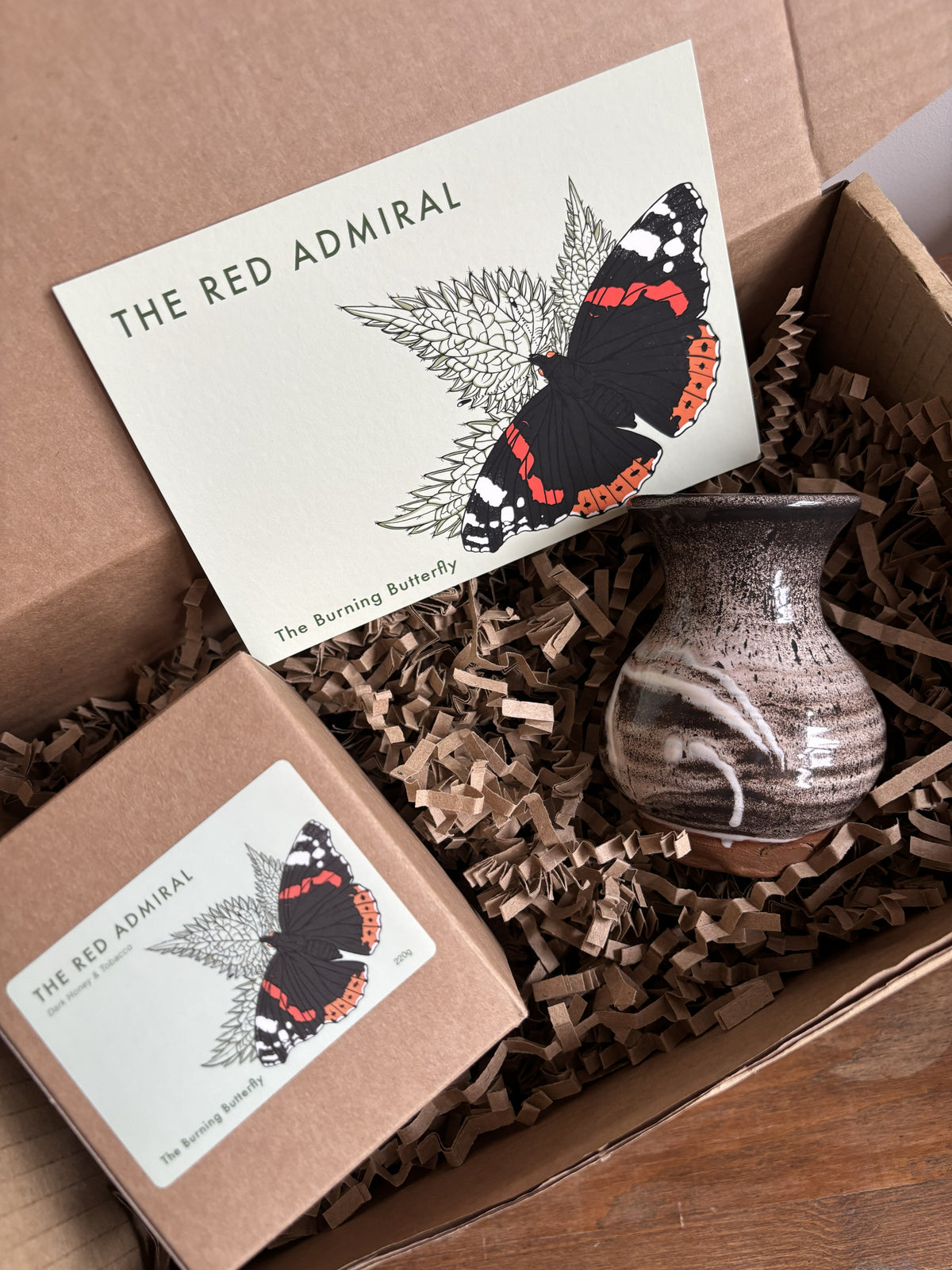 A gift box from The Burning Butterfly containing The Red Admiral candle in a kraft gift box, a small brown and white bud vase and The Red Admiral butterfly A6 postcard. 