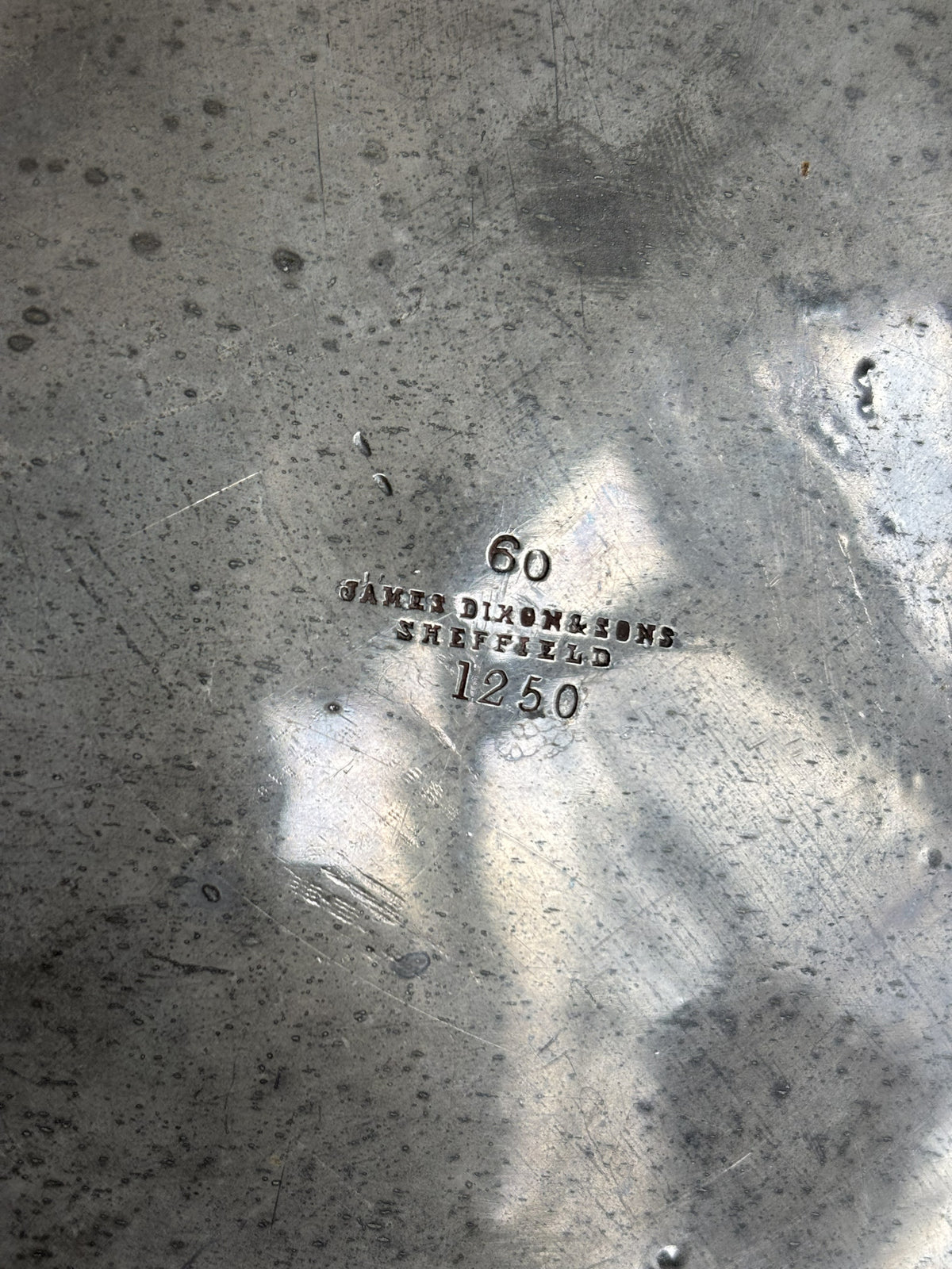 Close-up of a brushed metallic surface with stamped markings reading '60', 'James Dixon & Sons Sheffield', and '1250'