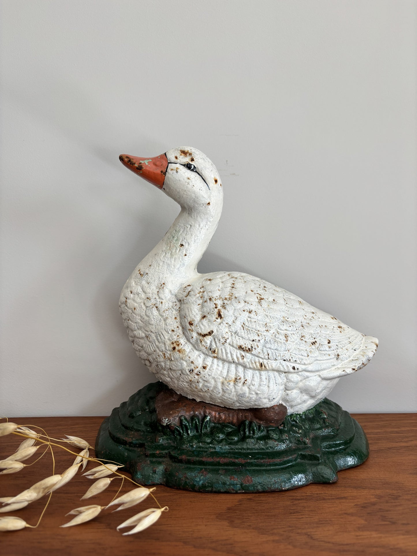 A decorative vintage cast iron white duck doorstop with a textured finish, perched on a dark green base, displayed on a wooden surface against a plain light gray wall.