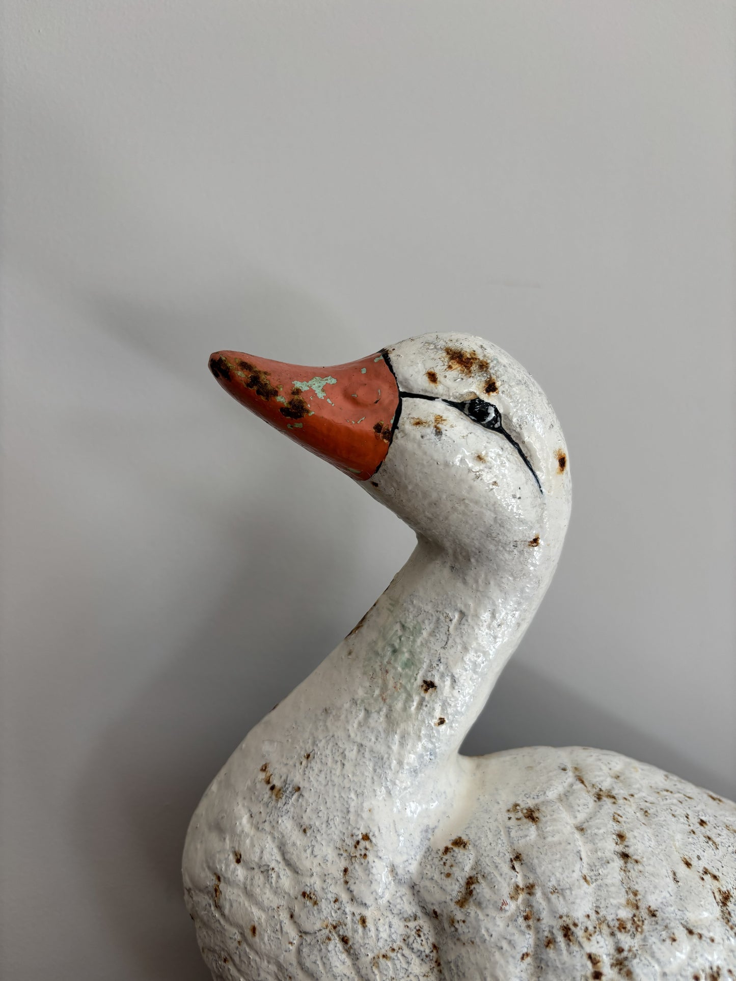 A close-up of a vintage white duck cast iron doorstop with a textured, weathered finish, featuring a reddish-orange beak and small brown speckles, set against a plain light gray background.