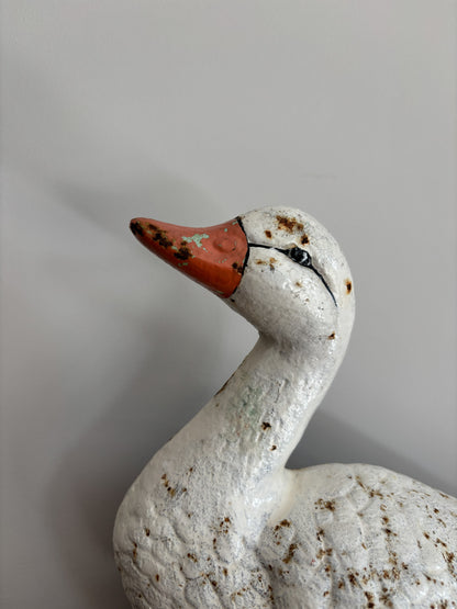 A close-up of a vintage white duck cast iron doorstop with a textured, weathered finish, featuring a reddish-orange beak and small brown speckles, set against a plain light gray background.