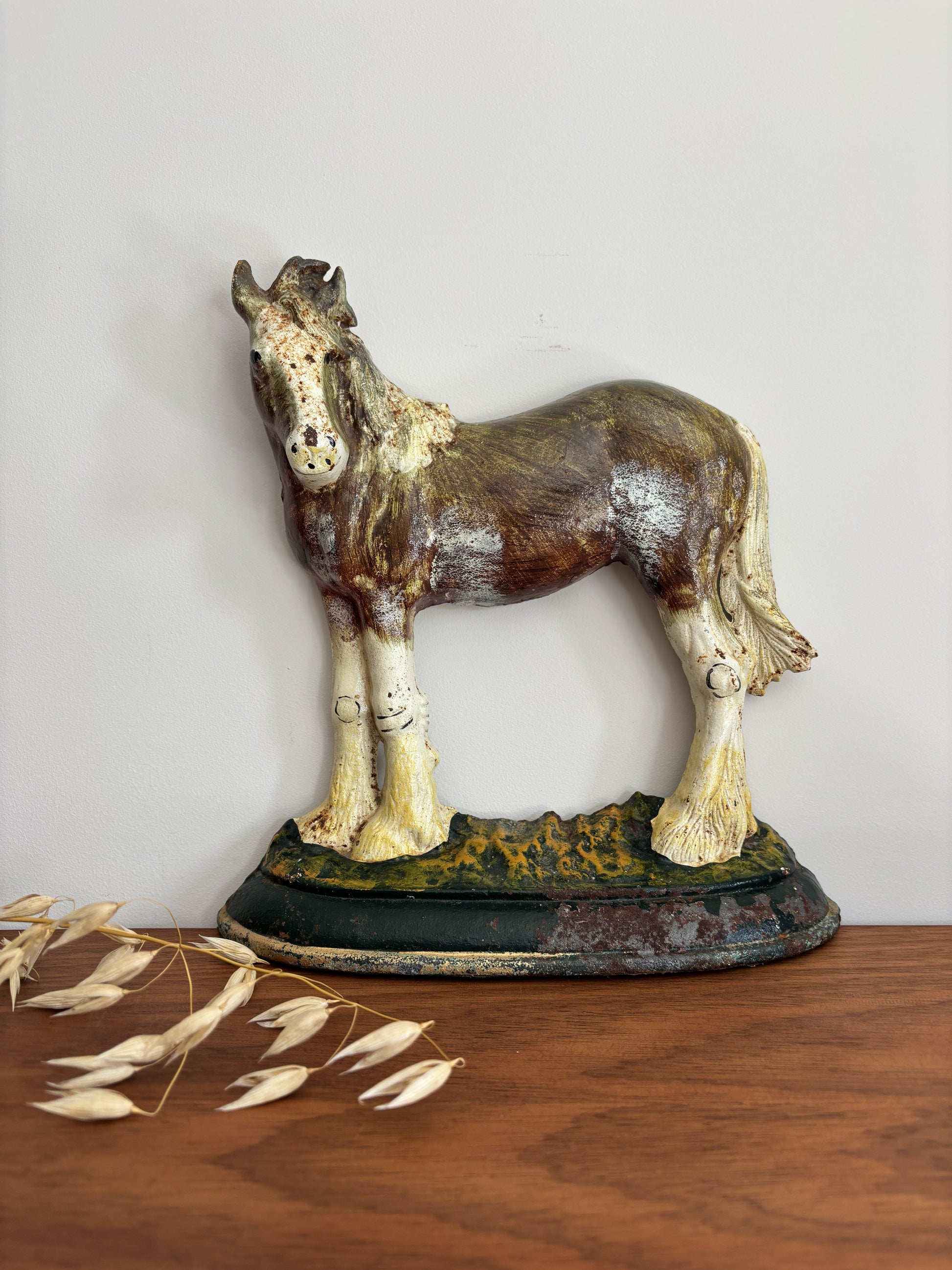 A vintage cast iron shire horse figurine doorstop standing on a decorative base, displayed on a wooden surface against a plain light wall.