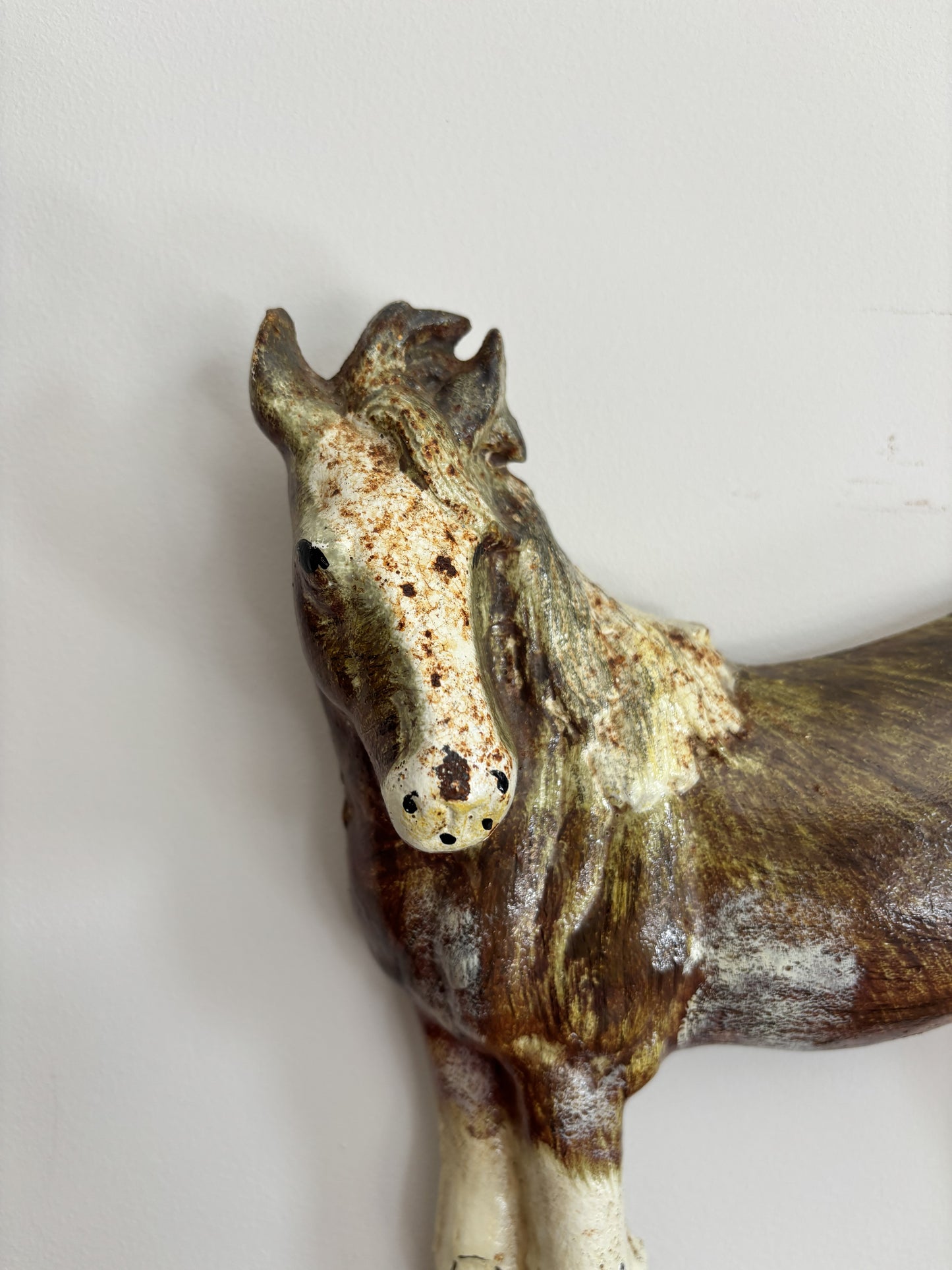 A vintage cast iron shire horse figurine doorstop standing on a decorative base, displayed on a wooden surface against a plain light wall.