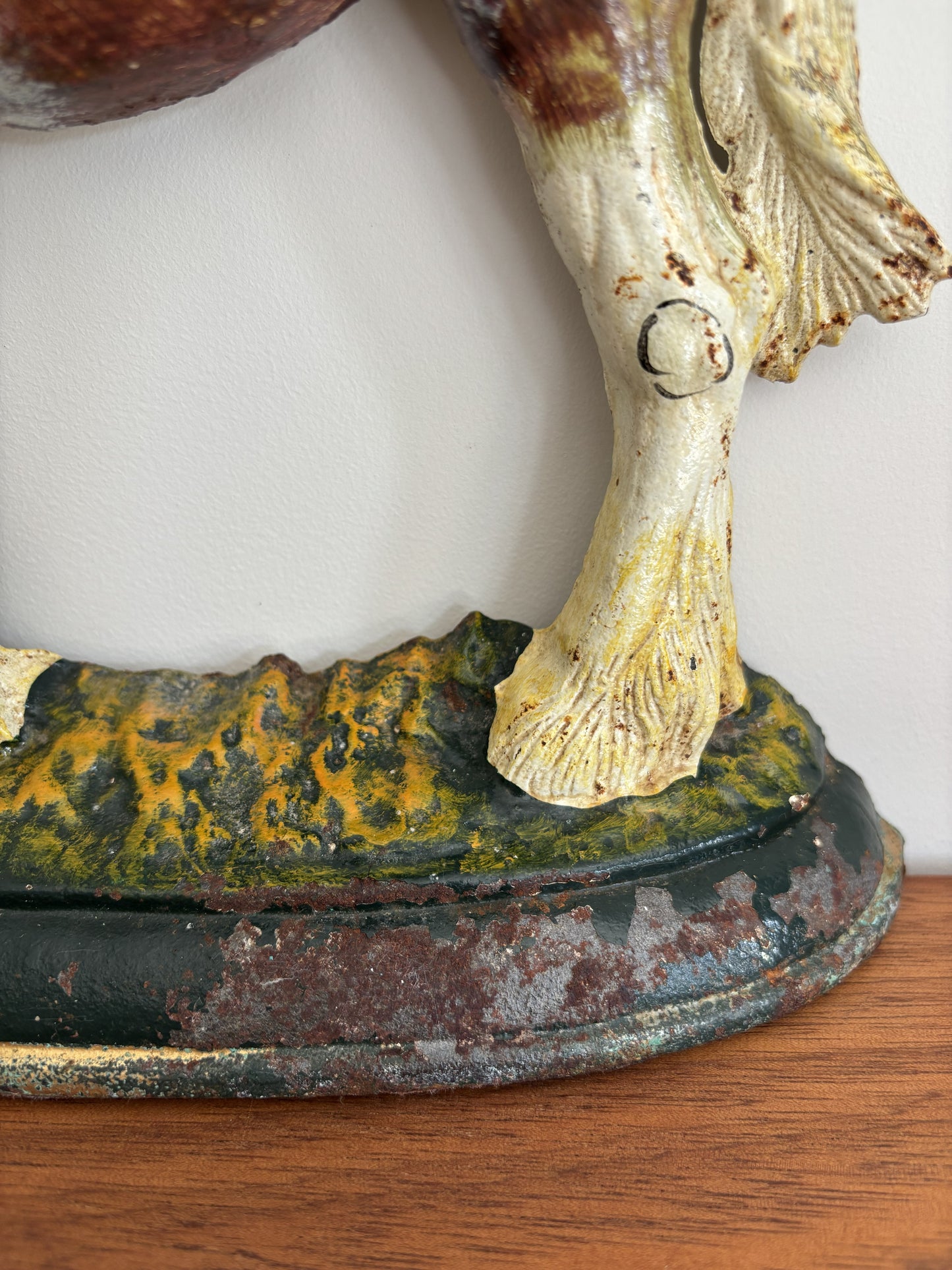 Close-up of a vintage cast iron shire horse figurine showing the lower leg and hoof, mounted on a weathered base with green, yellow, and dark patina details, resting on a wooden surface.