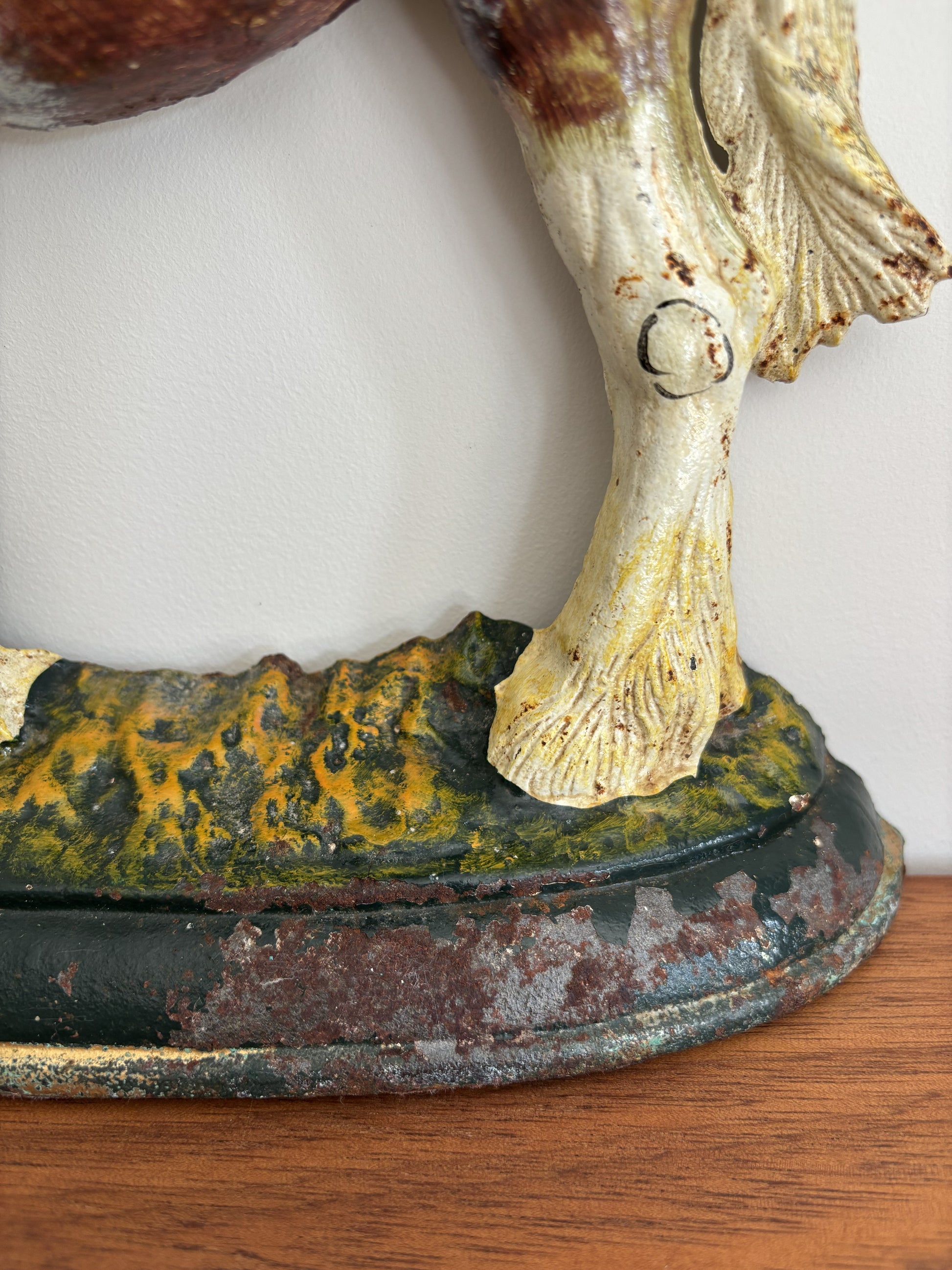 Close-up of a vintage cast iron shire horse figurine showing the lower leg and hoof, mounted on a weathered base with green, yellow, and dark patina details, resting on a wooden surface.
