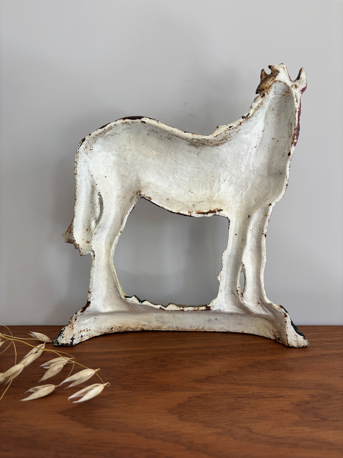 A distressed white horse-shaped decorative sculpture with a rustic, chipped finish, displayed on a wooden surface against a neutral gray background.