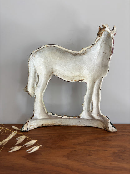 A distressed white horse-shaped decorative sculpture with a rustic, chipped finish, displayed on a wooden surface against a neutral gray background.