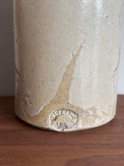 Close-up of a vintage stoneware bottle with a textured, glossy beige glaze and a makers mark