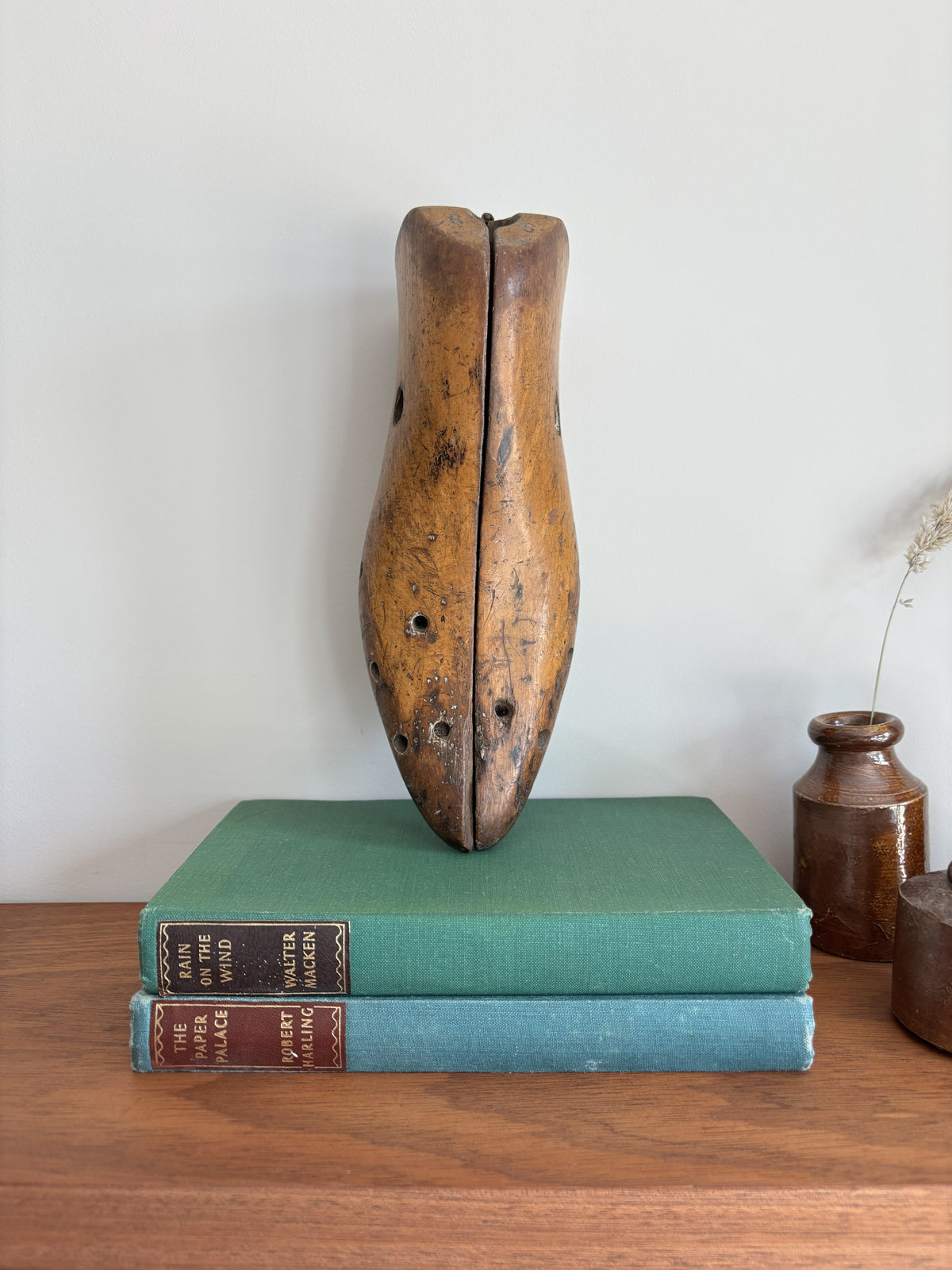 A vintage wooden shoe last stands upright on top of two stacked antique books on a wooden table against a plain light wall.