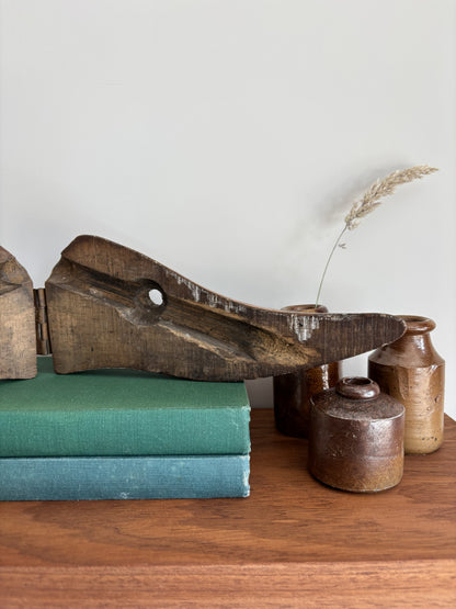 A vintage wooden shoe last with a circular hole, displayed on a stack of vintage green and teal books alongside small ceramic vases on a wooden shelf.