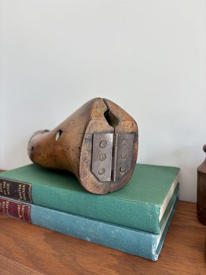 A vintage wooden shoe last with metal hinge rests on two stacked antique books on a wooden surface against a plain light wall.
