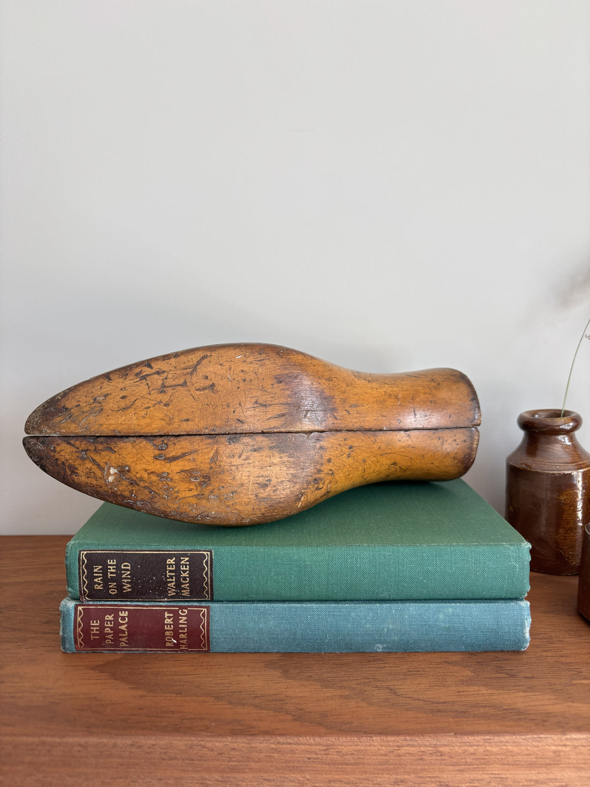 The bottom of a vintage wooden shoe last resting on two antique books on a wooden table against a plain wall.