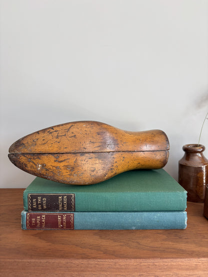The bottom of a vintage wooden shoe last resting on two antique books on a wooden table against a plain wall.