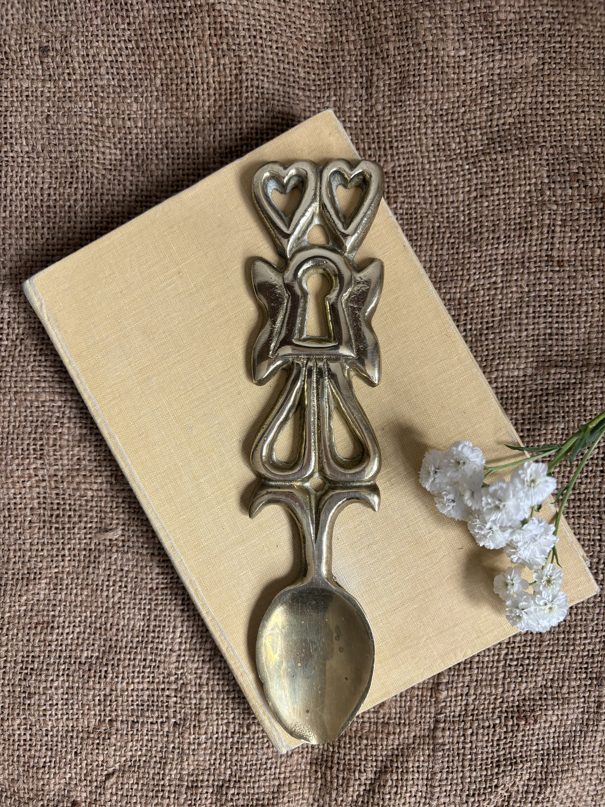 A vintage Welsh Brass Love Spoon resting on a cream book