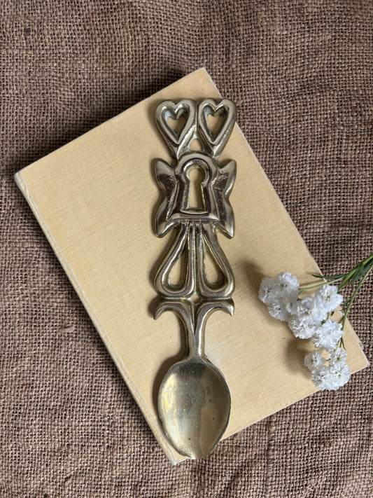 A vintage Welsh Brass Love Spoon resting on a cream book