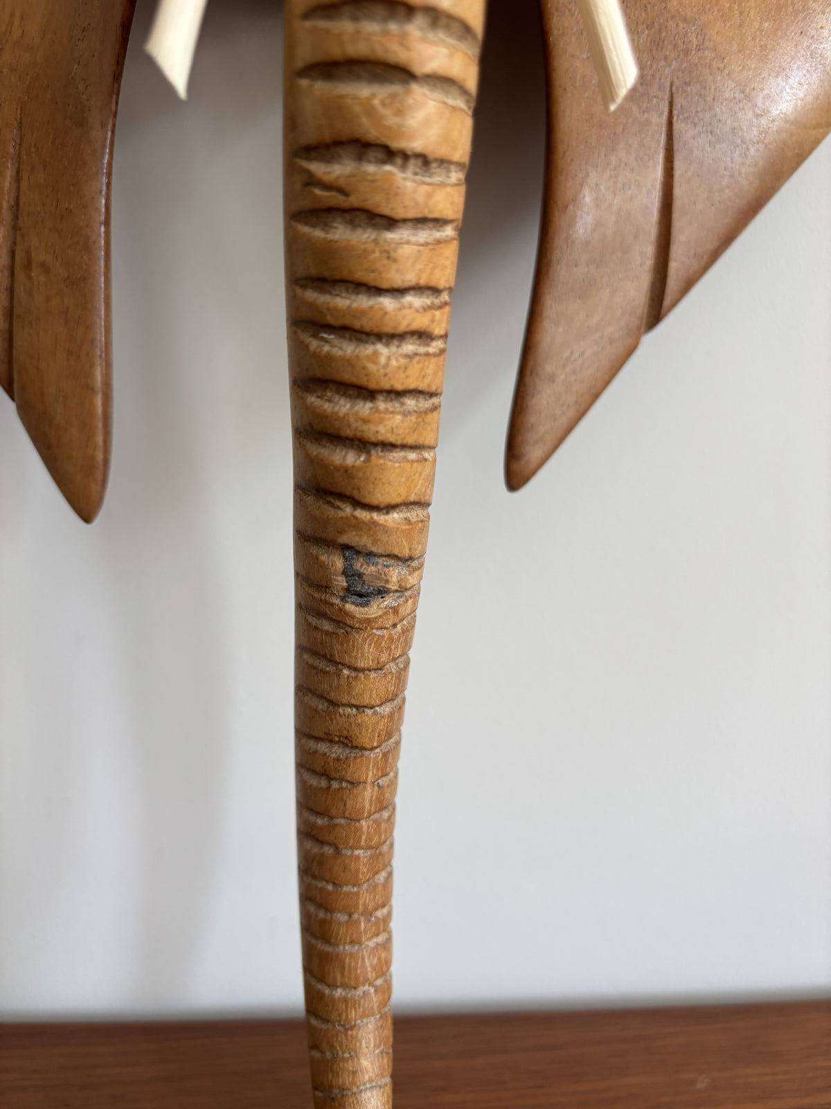 Close-up of a carved wooden elephant figurine showing the textured trunk and part of the ears against a plain light background.
