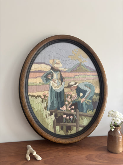 Round framed tapestry with pastoral scene on a wooden shelf.