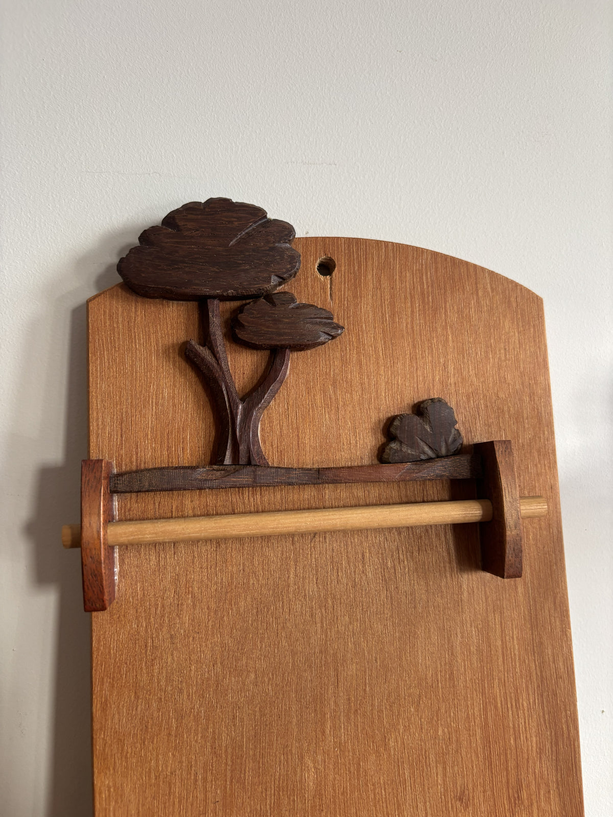 A vintage mid-century wooden notepad holder with a carved tree design on the backplate, mounted on a plain off-white wall.
